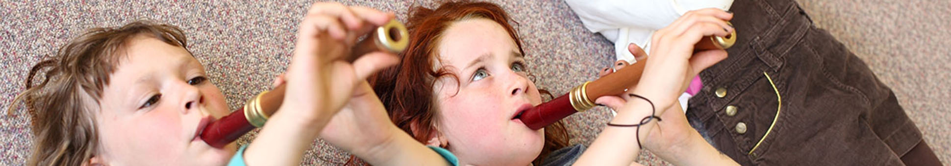 Drei Kinder spielen auf dem Boden liegend Blockflöte