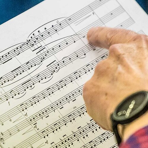 Hand einer Dirigentin zeigt auf eine Stelle im Notenblatt