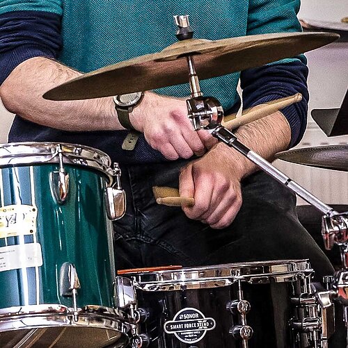 Drummer in der Bigbandprobe; auf einer Fensterscheibe im Hintergrund spiegelt sich der Rest der Band