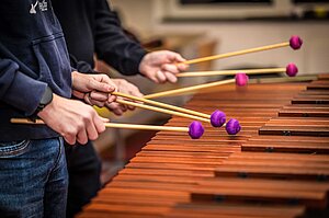 Die Hände von zwei Personen mit je drei Schlegeln im Marimba-Unterricht