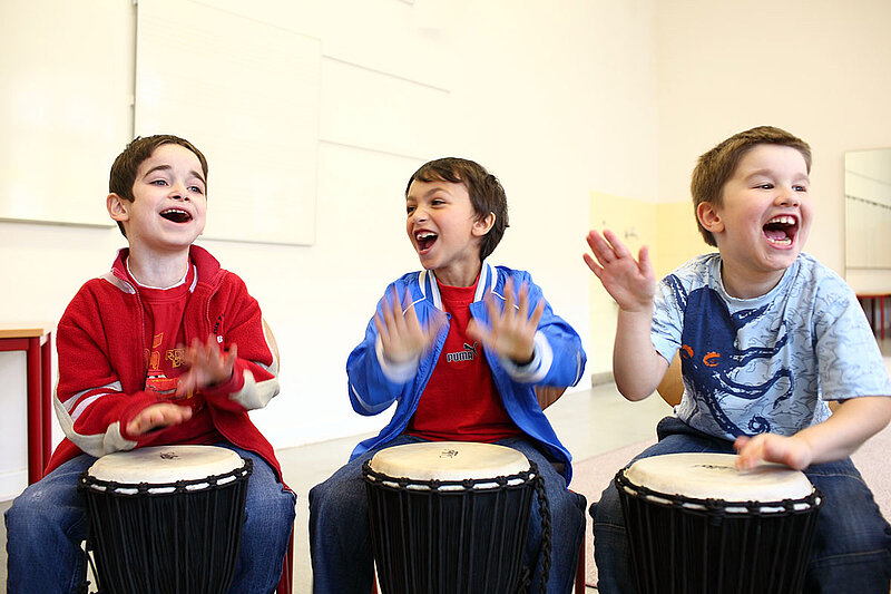Drei Jungen trommeln ausgelassen auf Djembés