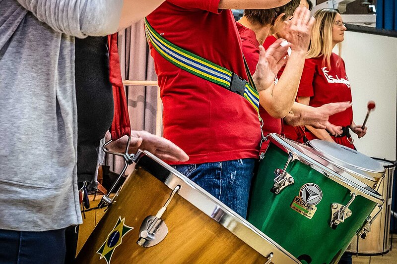 3 Timbal-Spielerinnen im Samba-Orchester holen synchron zum Schlag auf das Trommelfell aus.