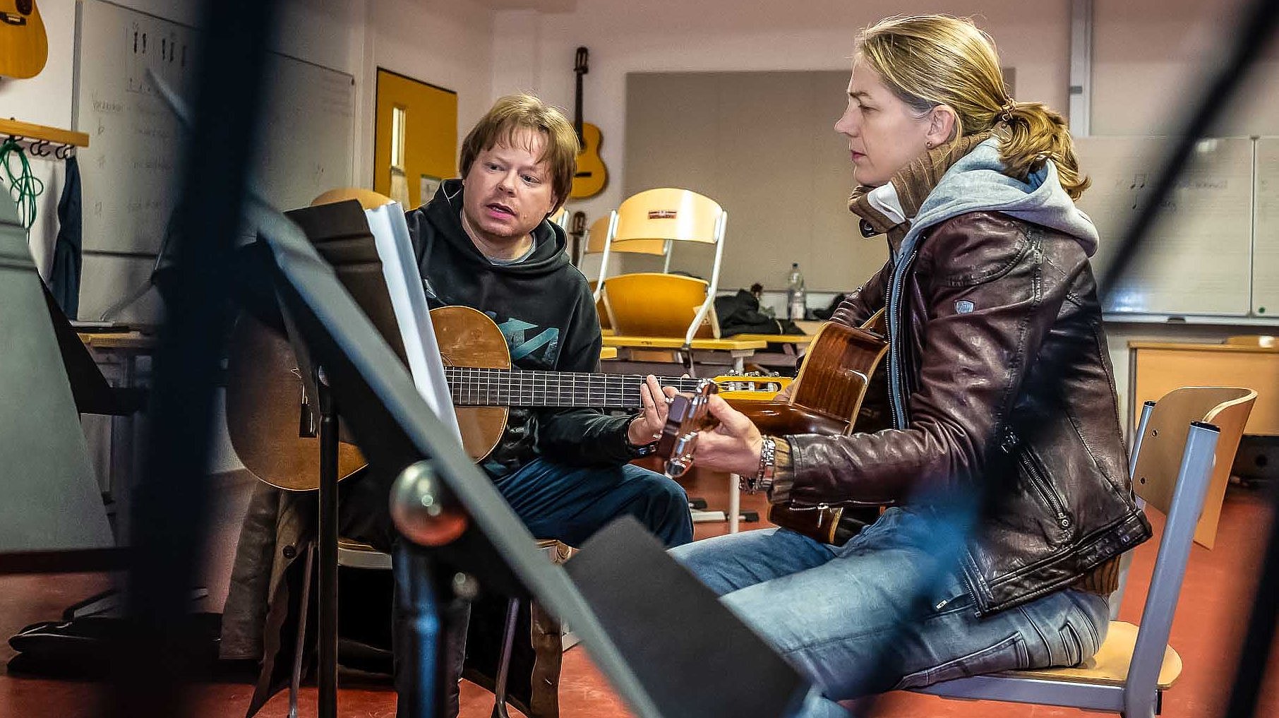 Erwachsene Gitarrenschülerin und Gitarrenlehrer spielen gemeinsam in einem Musikraum